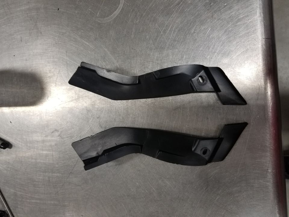 Two black plastic trim pieces on a brushed metal surface.
