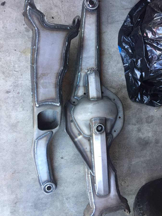 Two welded tubular metal suspension control arms on concrete floor