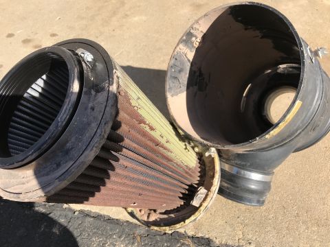 1989 Ford Bronco - A dirty, conical air filter element is shown next to its intake housing. The filter appears to be made of oiled cotton gauze and has a meta…