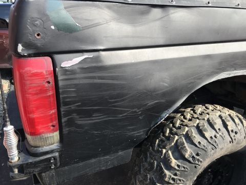 1989 Ford Bronco - The rear passenger side quarter panel and taillight of a black Ford Bronco are visible, showing significant scratches and some paint damage…