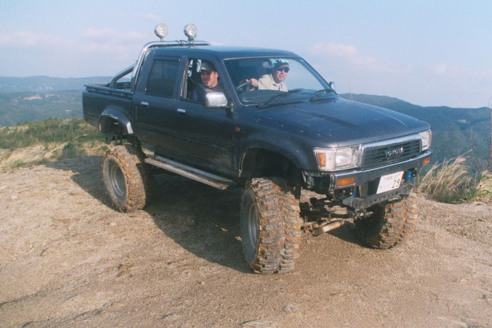 Lifted dark Toyota double-cab pickup on mud tires parked on a dirt overlook