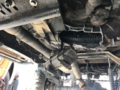 1989 Ford Bronco - The underside of a vehicle shows a damaged transfer case with a broken housing and exposed chain and gears. Drivelines and suspension compo…