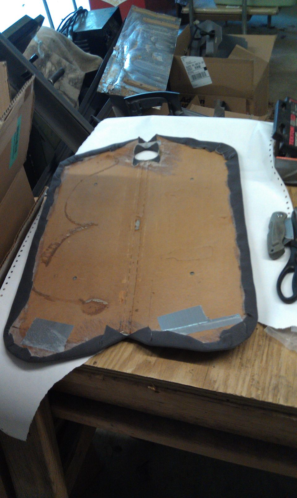 Automotive door panel with gray trim and a cutout, on a workbench.