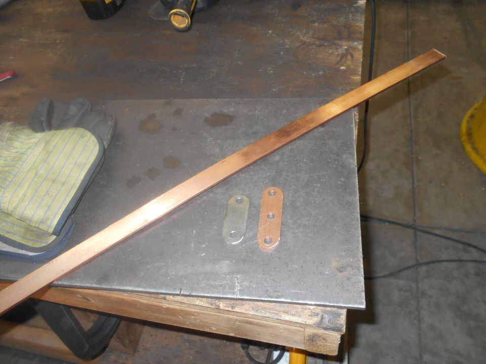 Copper bar and metal plates on a workbench with work gloves.