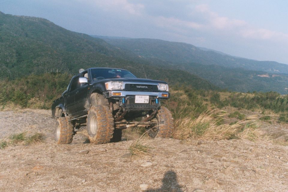Lifted dark Toyota pickup on oversized off-road tires atop a dirt hill with mountains behind.