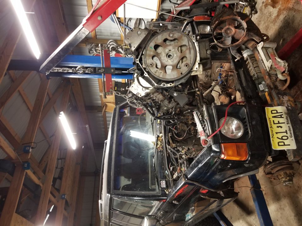 Black Mitsubishi Montero SUV with engine removed, suspended by engine hoist in a garage.