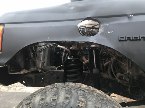 1989 Ford Bronco - A close-up view of the rear fender well of a gray Ford Bronco showing modifications. A circular opening has been cut into the body above th…