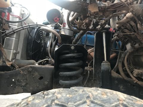 1989 Ford Bronco - A close-up, low-angle view of the front suspension and engine bay of a vehicle, showing a large black coil spring, a shock absorber, and va…