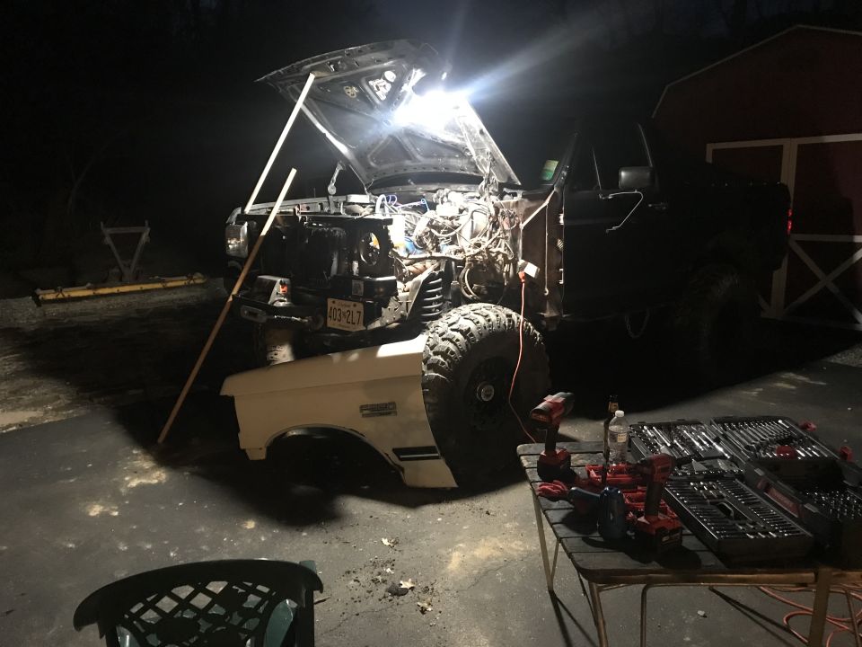 1989 Ford Bronco with hood open, engine exposed, tools on table at night.