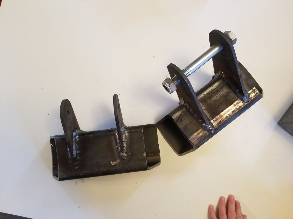 Two custom metal brackets with welded seams and bolt hardware on a white surface.