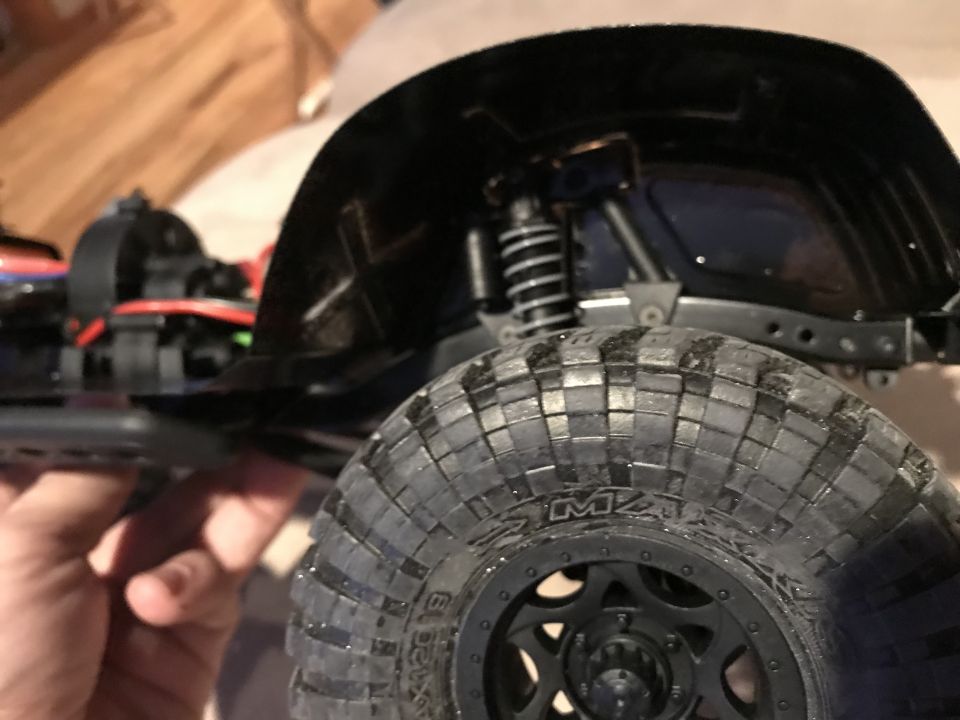 Hand holding underside of an RC crawler showing chassis and mud tire