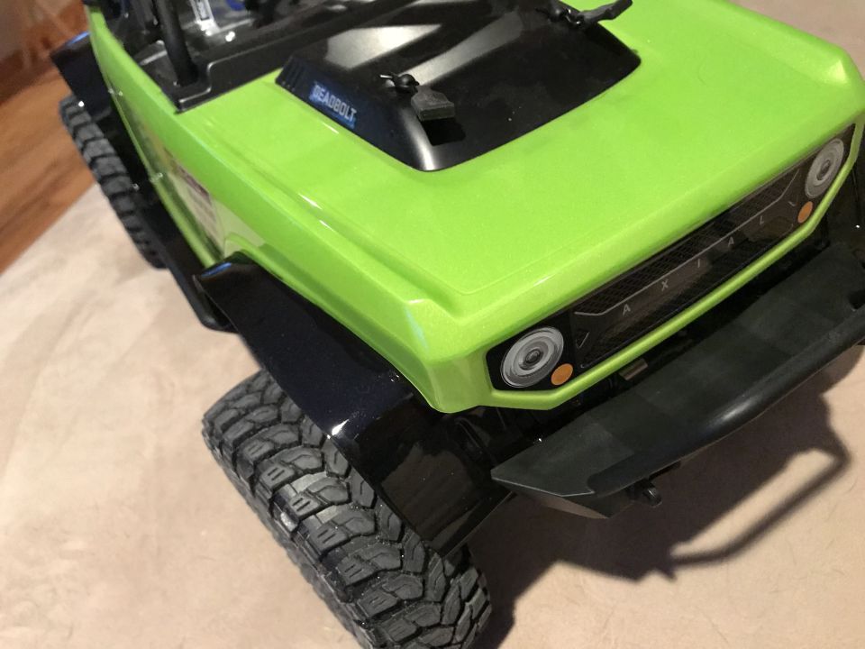 Green RC rock crawler with black fender flares and bumper, showing the front grille.