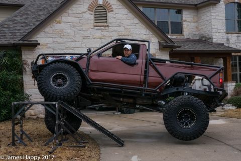 1989 Ford Bronco - Modified pickup truck with extensive roll cage and off-road tires is positioned on a ramp.