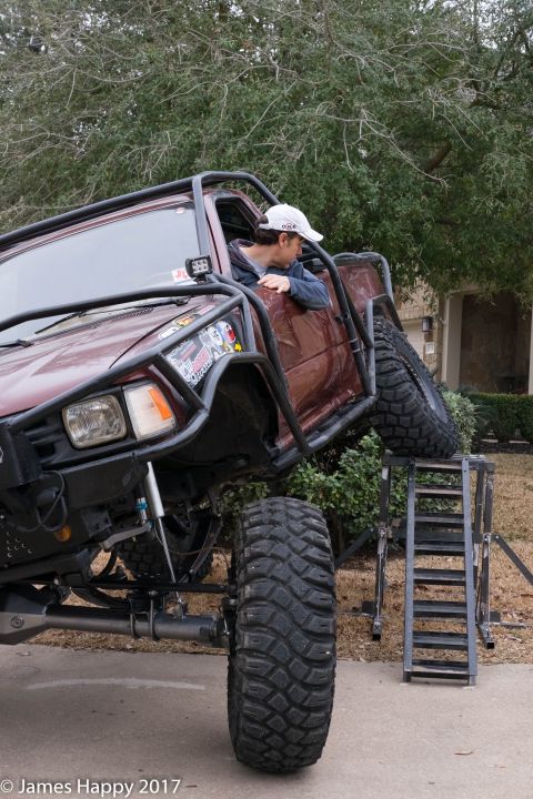 1989 Ford Bronco - A heavily modified maroon truck with oversized tires is positioned on a ramp, its off-road capabilities.