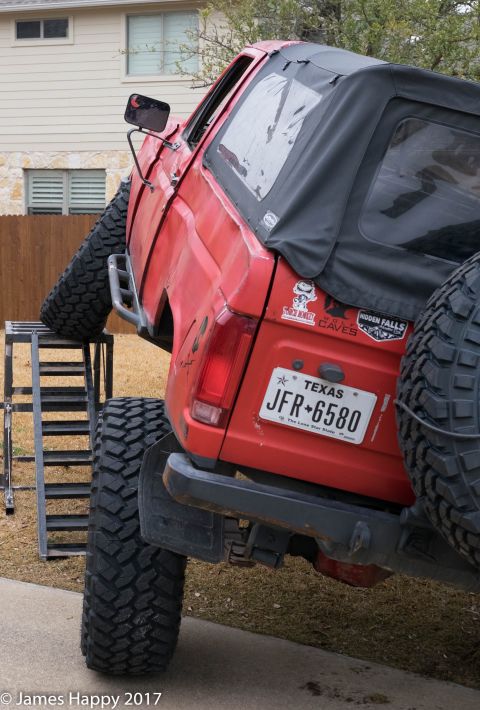 1989 Ford Bronco - This red SUV has a soft top and is heavily modified with off-road tires and a lifted suspension.