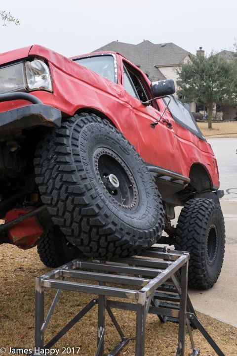 1989 Ford Bronco - This red SUV, likely from the early 1990s, is positioned on a metal ramp, its off-road capabilities with oversized tires.