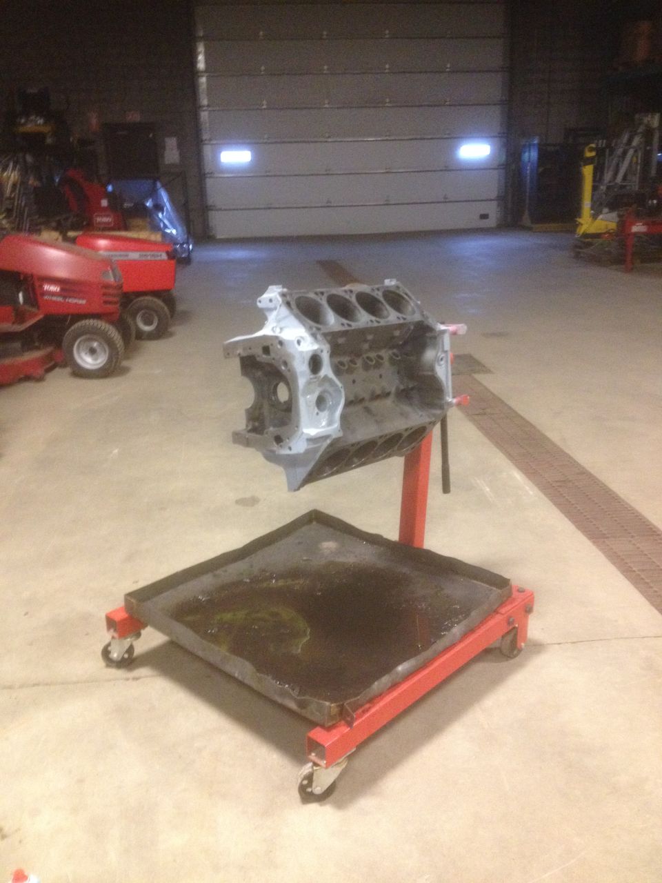 Engine block on a red rolling stand with a drip pan underneath, in a garage