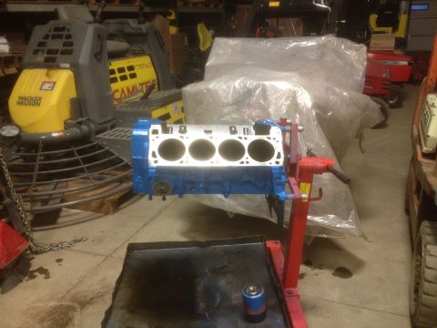 1979 Ford Bronco - A blue engine block is mounted on a red stand in a workshop setting, surrounded by construction equipment.