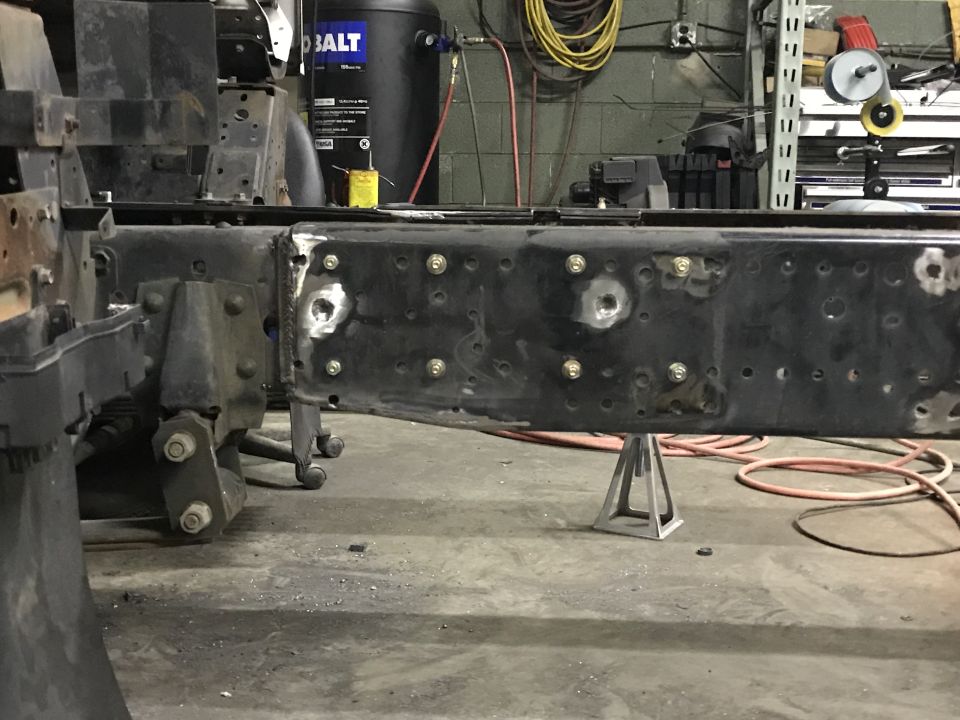 Close-up of a heavy-duty truck frame section, supported by jack stands, with visible bolts and welds