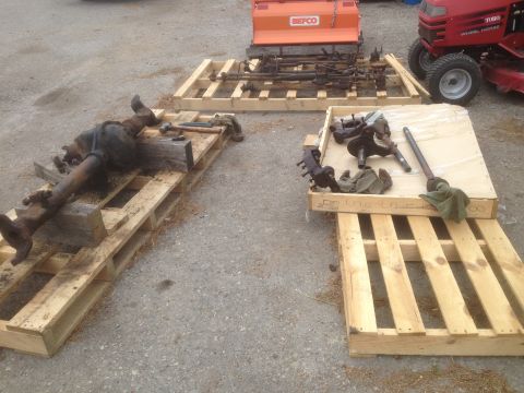 1979 Ford Bronco - Various vehicle axles and suspension parts are organized on pallets, ready for transport or storage.