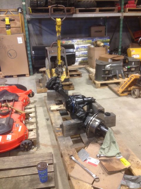 1979 Ford Bronco - An axle assembly sits on pallets in a warehouse, alongside a lawnmower and other equipment.