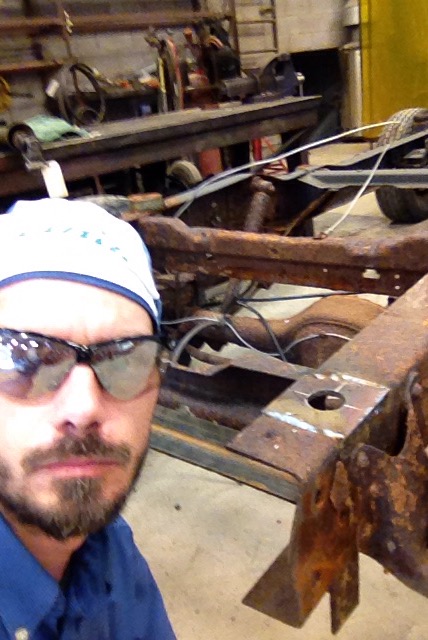 1979 Ford Bronco - Workshop scene with a person and a heavily rusted vehicle frame.