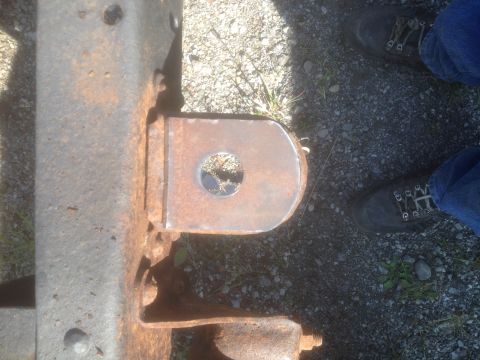 1979 Ford Bronco - Close-up of a rusty metal bracket on a vehicle frame, with a person's feet in the background.