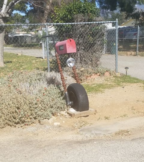 1990 Ford Bronco - Unique mailbox constructed from a tire, pipes, and a headlight, situated outdoors.