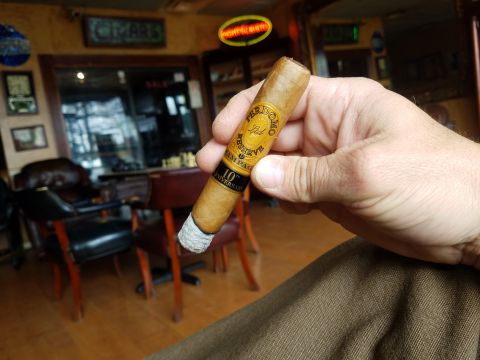 2018 Ford Bronco - A hand holds a Perdomo 10th Anniversary cigar in a dimly lit cigar lounge.