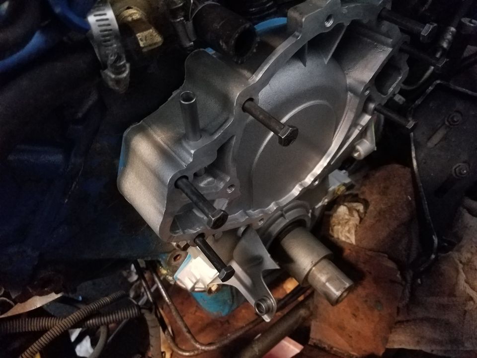 Close-up of a water pump assembly with bolts attached, surrounded by engine components