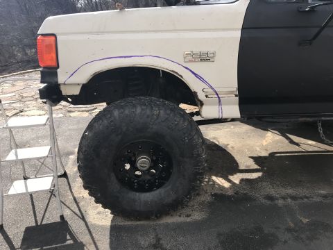 1989 Ford Bronco - A white and black Ford F-250 truck fender is marked with purple lines, showing a large off-road tire and a ladder nearby.