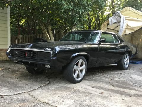 1969 Mercury Cougar - A black 1969 Mercury Cougar is parked in a driveway, showing its distinctive front grille and body style.