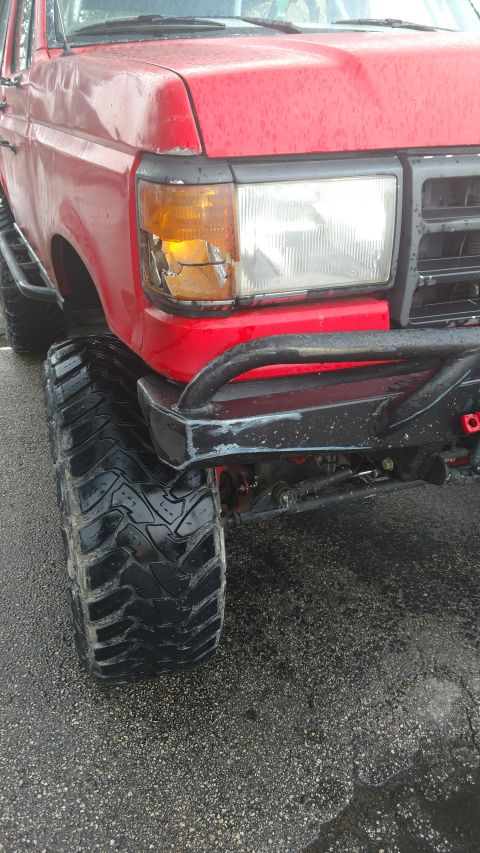 1989 Ford Bronco - Front corner of a red 1989 Ford Bronco showing large tires and a broken headlight assembly.
