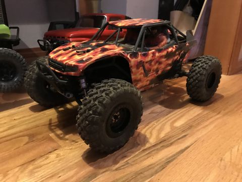 1989 Ford Bronco - RC rock crawler with flame graphics is shown indoors next to other vehicles.