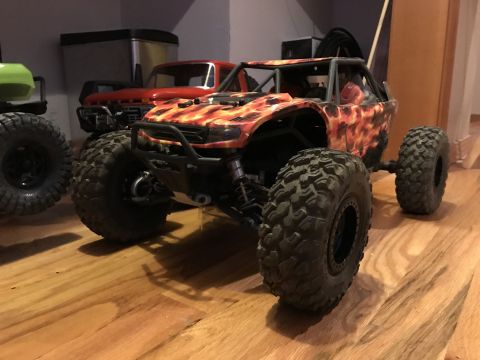 1989 Ford Bronco - This remote-controlled rock crawler features a flame graphic body and sits on a wooden floor next to other RC vehicles.