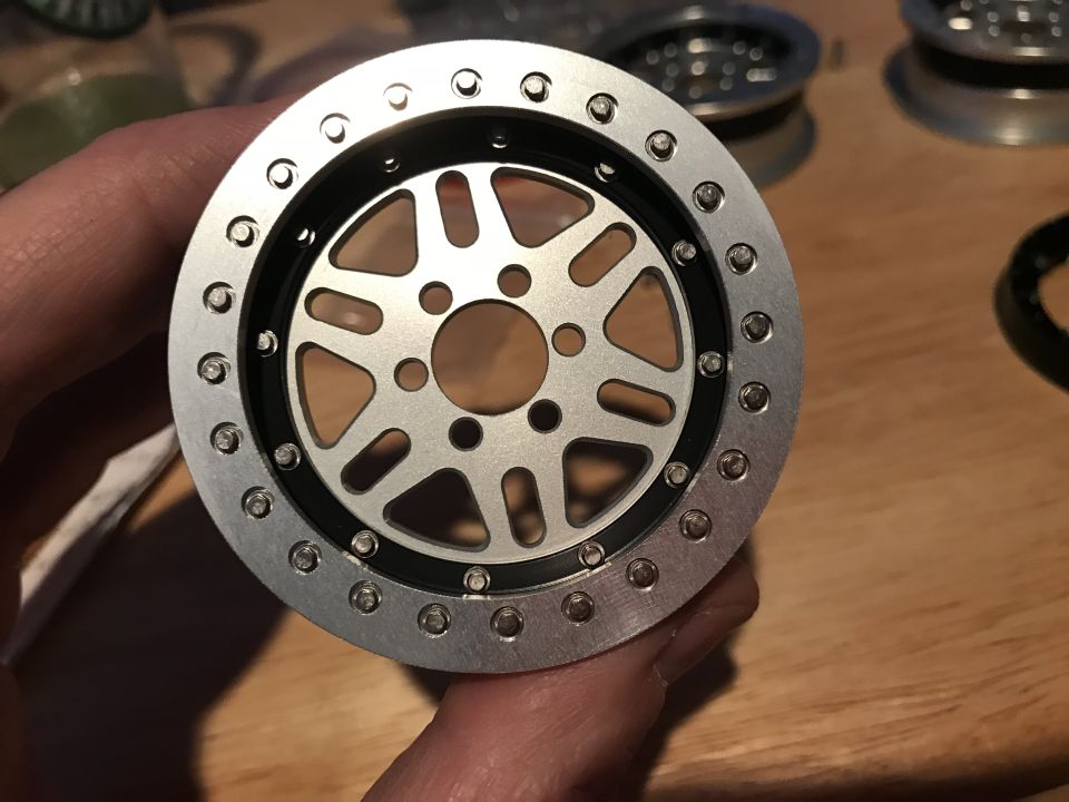 Silver metal wheel rim with black accent and numerous small bolts around the edge, held by a hand