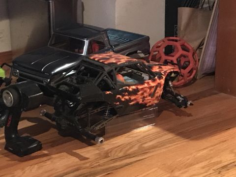 1989 Ford Bronco - A remote control rock crawler with flame graphics sits next to a separate truck body, with a controller in the foreground.