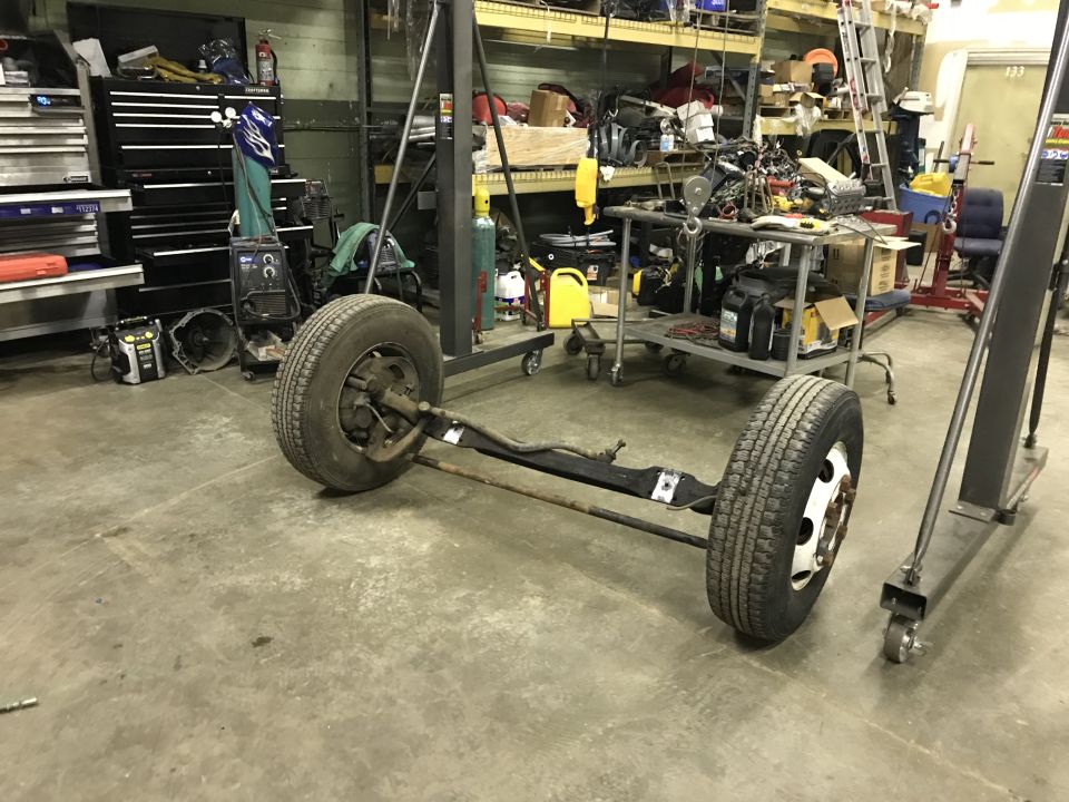 Front axle assembly with wheels and tires, in a workshop setting