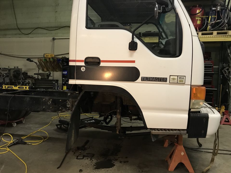 White truck cab on jack stands, front fender removed, showing "Tiltmaster" and "W4" badges