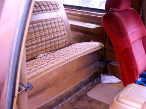 1980 Ford Bronco - The interior of a vehicle shows patterned brown bench seats and a red bucket seat, with a view out the window.
