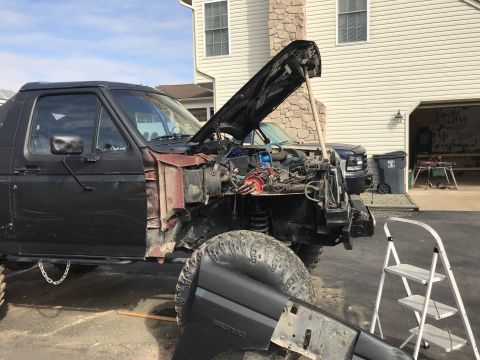 1989 Ford Bronco - A black 1989 Ford Bronco is shown with its hood open and front end disassembled, parked in a driveway.