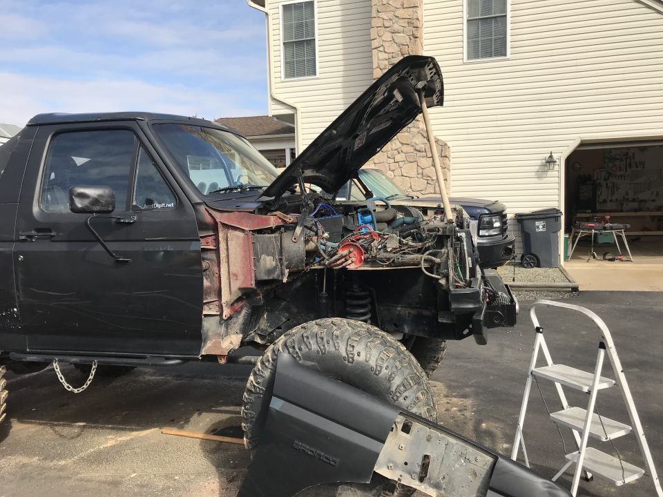 Black 1989 Ford Bronco with hood open and front end disassembled, parked in a driveway