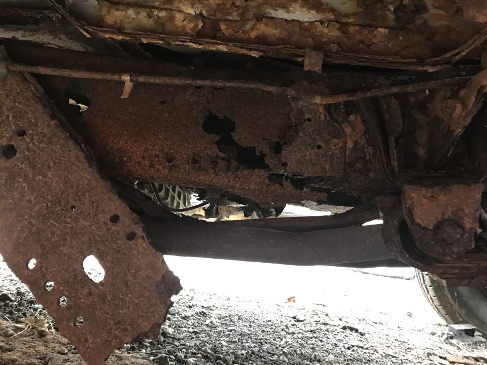 Heavily rusted vehicle frame and undercarriage with holes. Supermotors.net logo visible