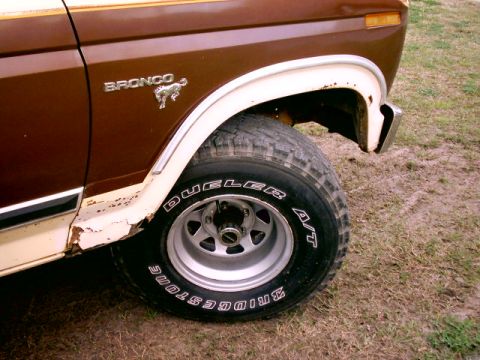 1980 Ford Bronco - Close-up of the front fender and wheel of a brown Ford Bronco, showing some rust and wear.