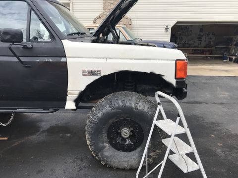 1989 Ford Bronco - This Ford F-250 appears to be undergoing repairs or modifications, with its hood open and a large off-road tire visible. A ladder is positi…
