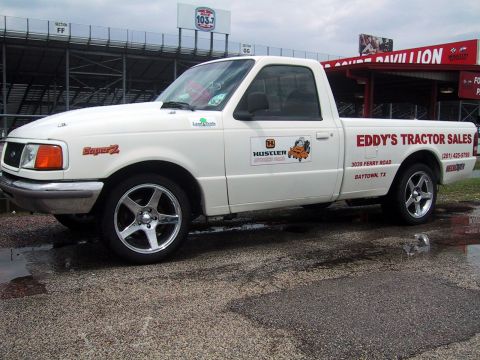 1969 Mercury Cougar - White pickup truck with business decals parked outdoors near a stadium structure.