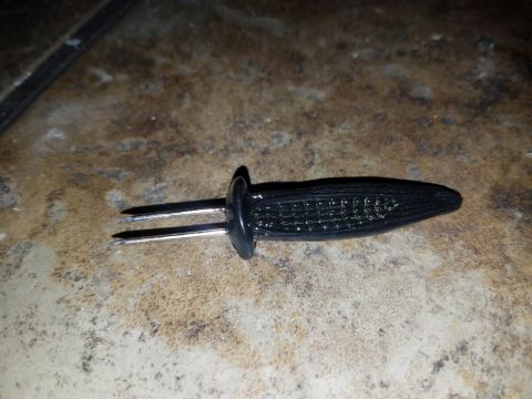 2018 Ford Bronco - A black corn cob skewer with two metal prongs rests on a speckled surface.
