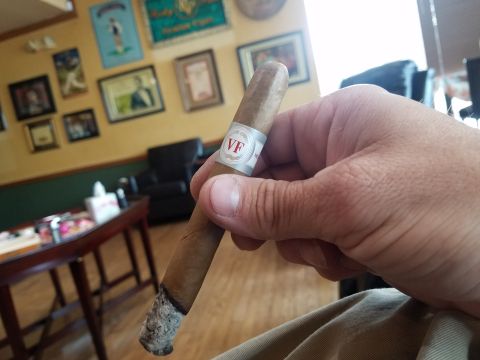 2018 Ford Bronco - A hand holds a lit cigar with a VF band in a room with framed pictures on the wall.