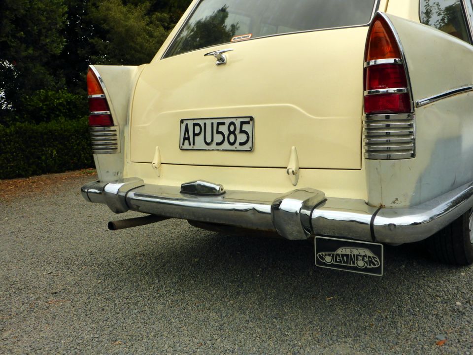 Rear of a cream-colored vintage car with chrome bumper, horizontal taillights, and license plate APU585