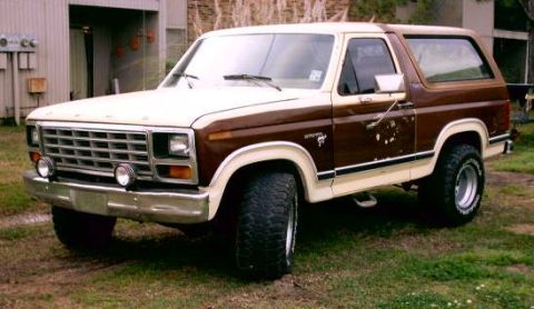 1980 Ford Bronco - This two-tone brown and cream Ford Bronco is parked on grass in front of a building.